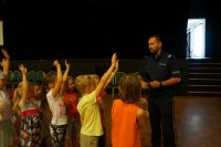 policjant stoi przed dziećmi, które podnoszą ręce i zgłaszają się do odpowiedzi