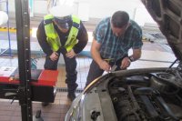 policjant  i pracownik stacji diagnostycznej sprawdzają oświetlenie w samochodzie