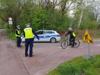 policjanci stoją na wprost radiowozu i kontrolują rowerzystę