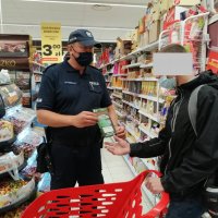 policjant wręcza klientowi sklepu ulotkę dotyczącą unikania zagrożeń związanych z koronawirusem
