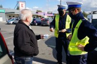 policjanci z ruchu drogowego wręczają seniorowi naklejkę na parkingu