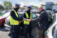 policjanci z ruchu drogowego wręczają seniorowi naklejkę na parkingu