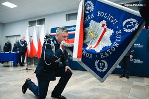 na zdjęciu Komendant Wojewódzki Policji w Katowicach klęczy i całuje sztandar