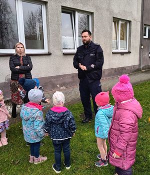na zdjęciu policjant stoi przed przedszkolem z dziećmi